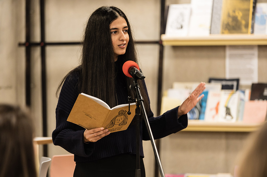 A girl holding a notebook speaking into a microphone.