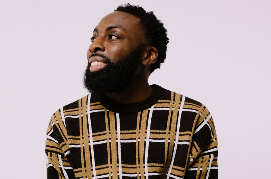 A man (Aniefiok Ekpoudom) wearing a checked jumper looking to the left.
