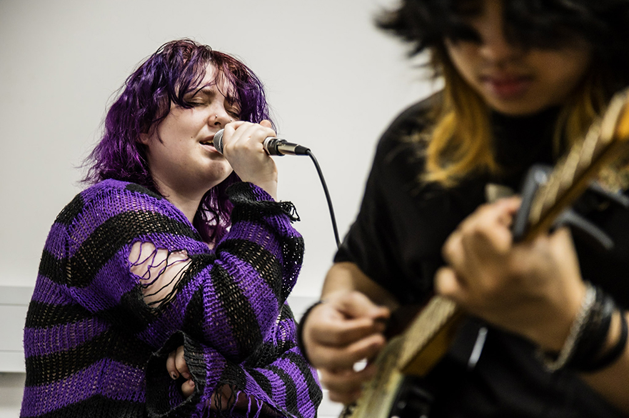 A girl singing into a microphone and a boy playing the electric guitar.