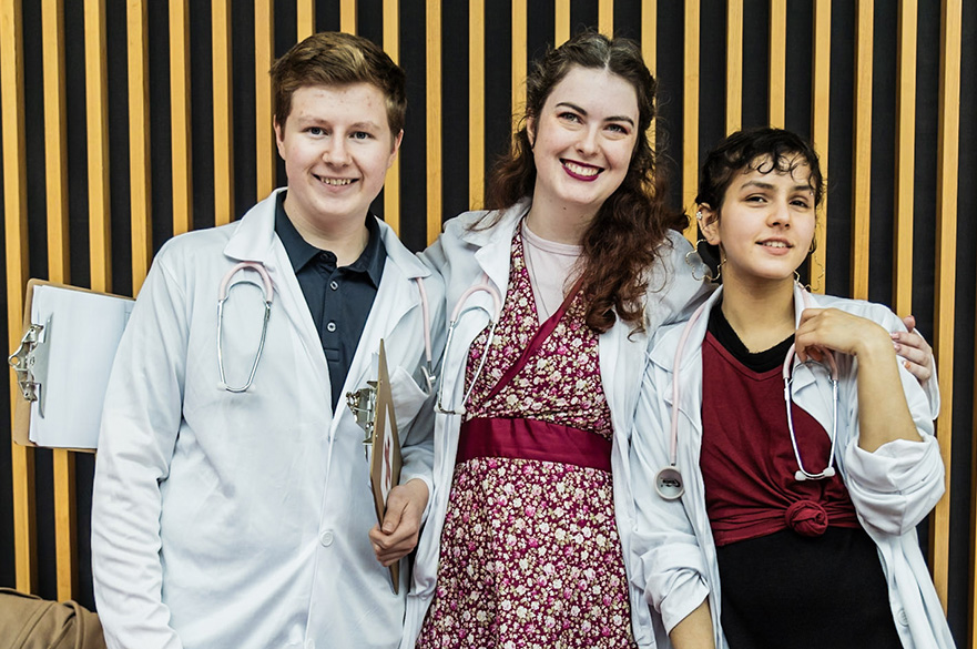 Three students stood with doctors coats on a stethoscopes around their necks.