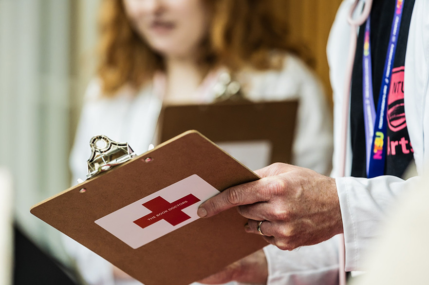 Someone holding a clipboard with a red cross on the back and the words Book Doctors.