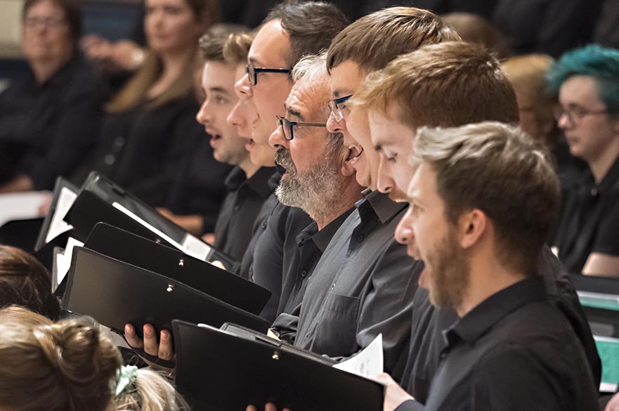 Men holding choir folders singing on stage.