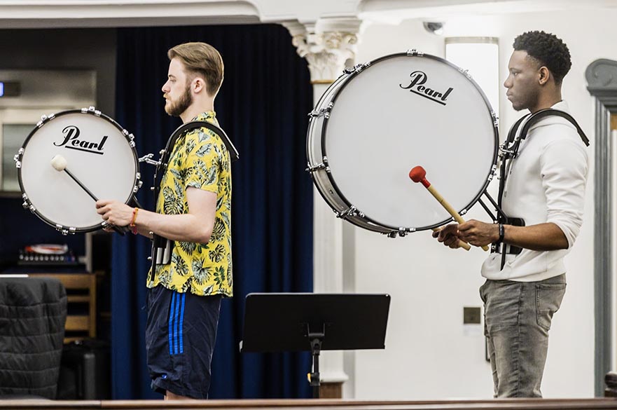 Two male students playing concert bass drums.