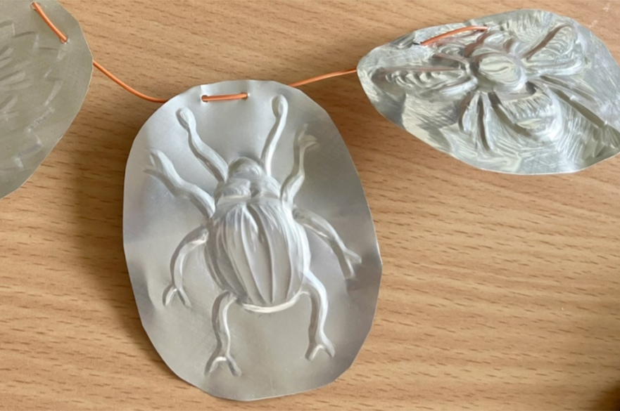 A piece of wire with three foil discs embossed with insects.