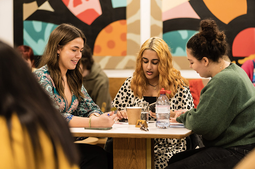Three female students sat around a table writing.