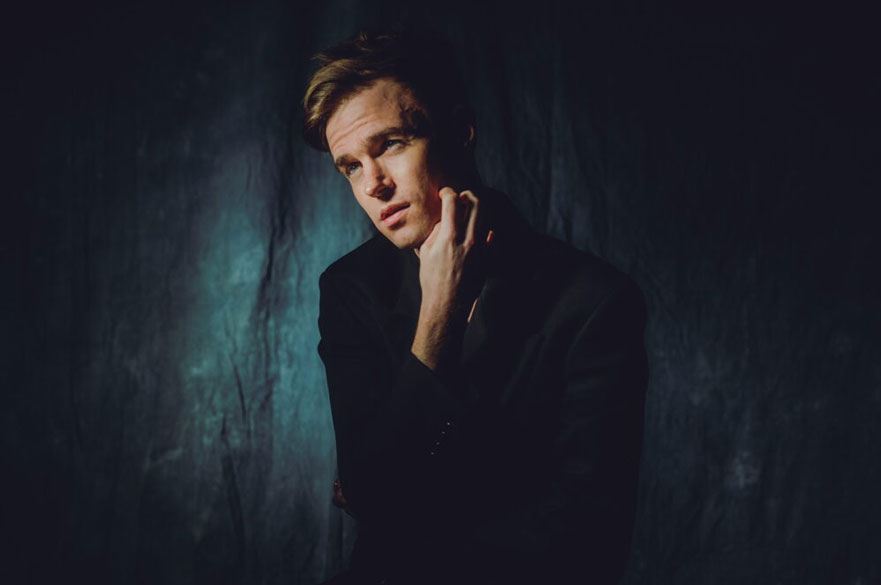 A young man standing against a dark background.