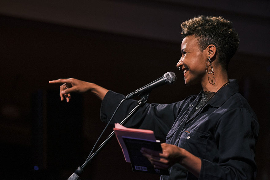 A woman on stage, pointing and smiling.