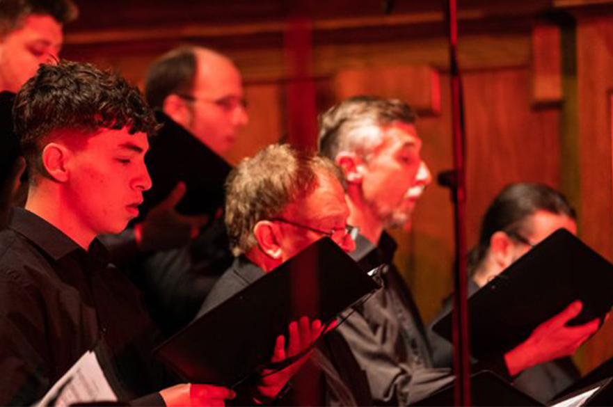 A group of male singers holding their music in choir folders during a concert.