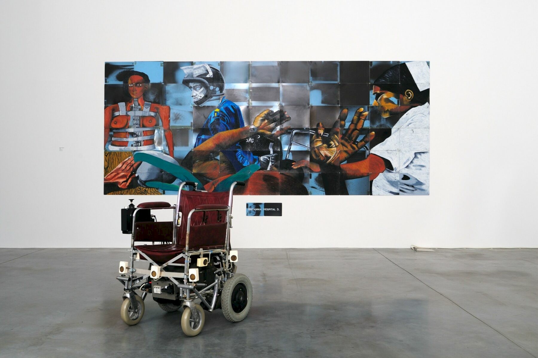 A wheelchair in front of an art exhibition by Donald Rodney.