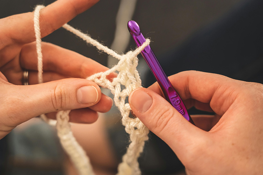 A pair of hands crocheting a piece of yarn.