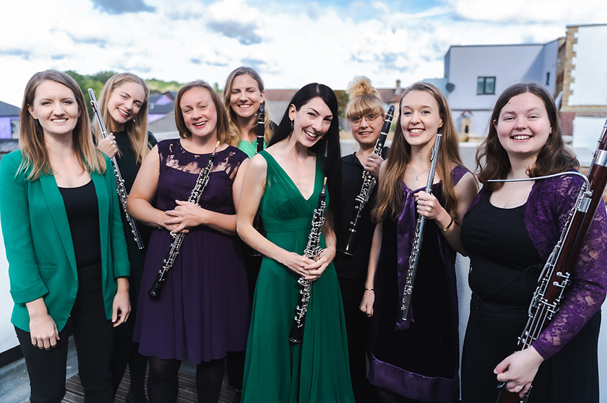 A group of female musicians holding their wind instruments smiling at the camera.