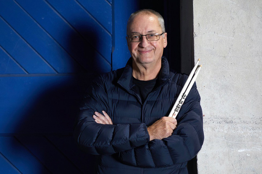 Allan Cox wearing a puffer jacker and holding a drum kit.
