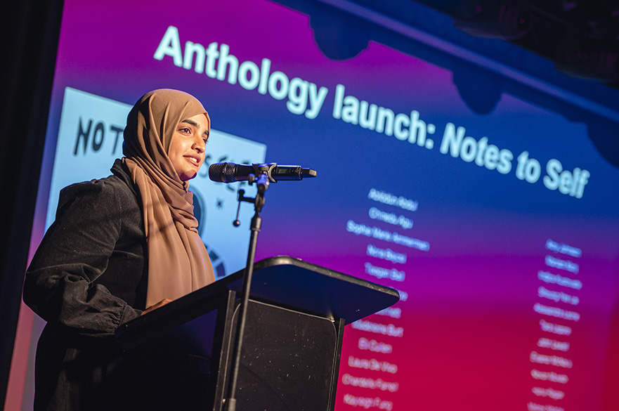 A young woman stood on a stage talking into a microphone.