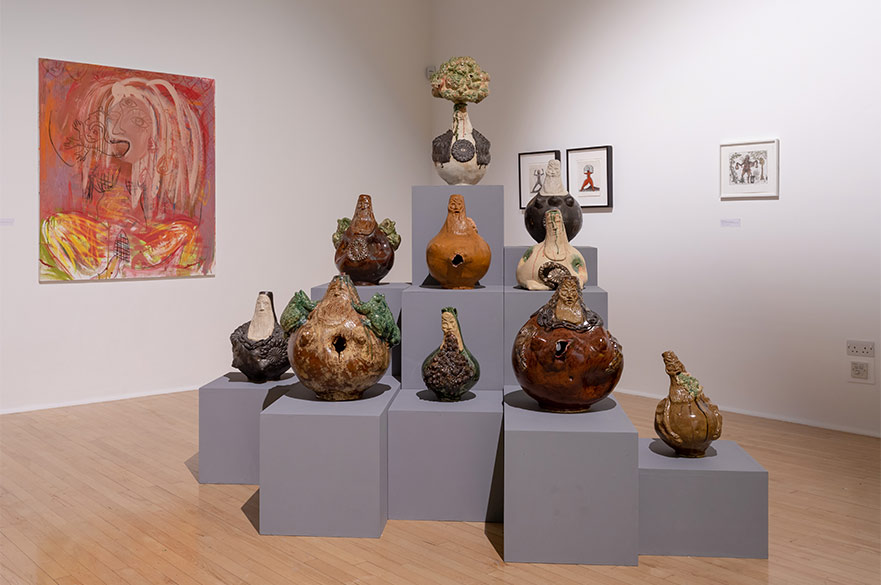 A collection of sculptures on plinth in a gallery with framed artwork on the walls.