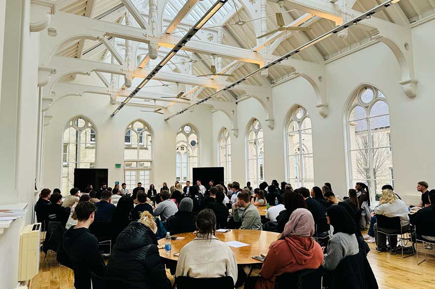 Students sat around round tables looking towards a panel of alumni