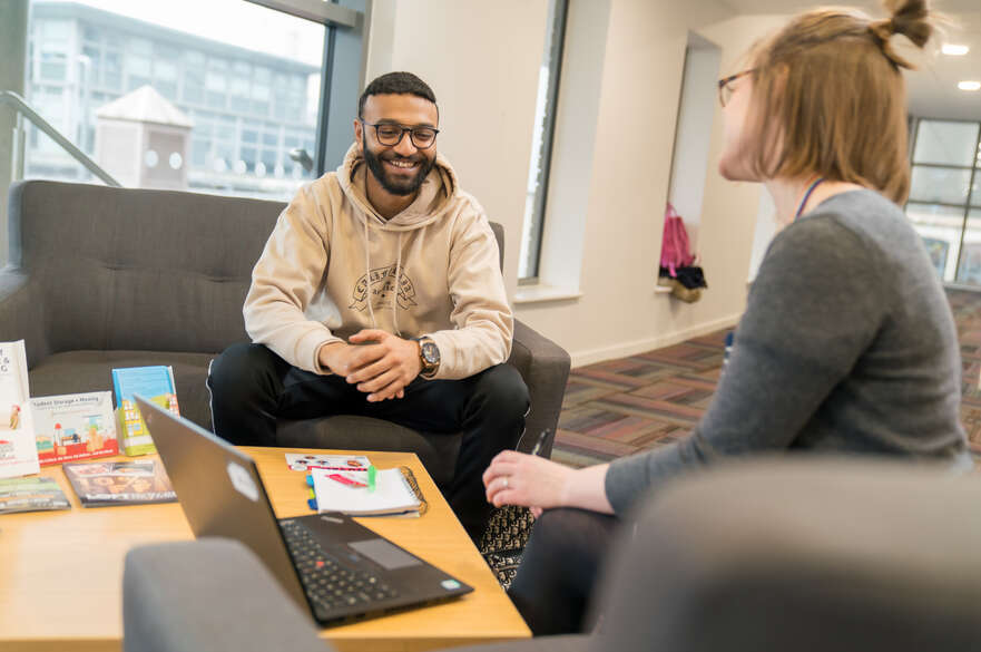 A student sat on a sofa chatting to a member of NTU staff.
