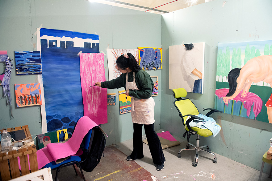 A student painting in a studio with lots of other artwork around.