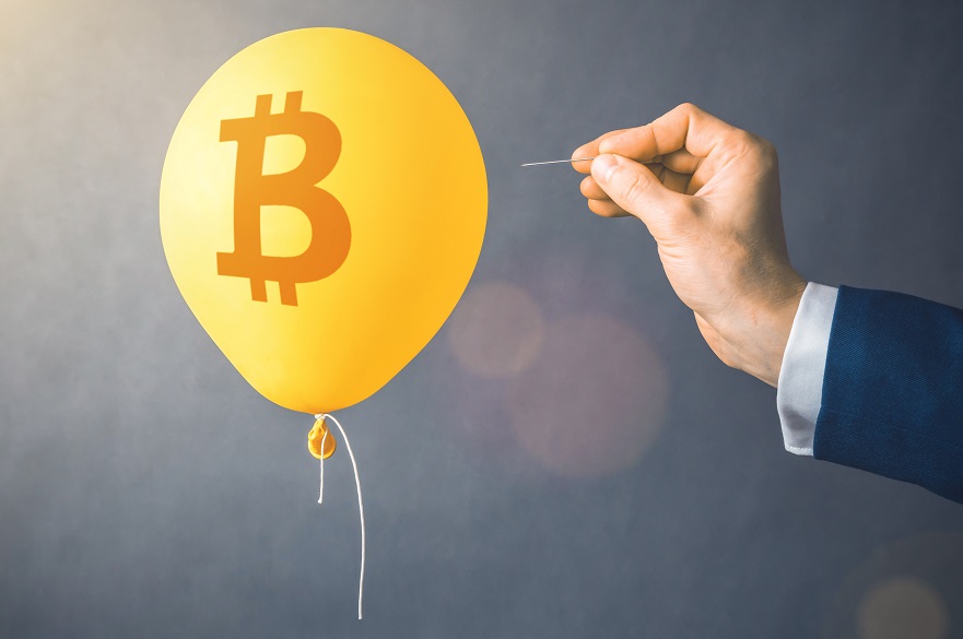 Hand about to pop a bitcoin logo balloon with a needle
