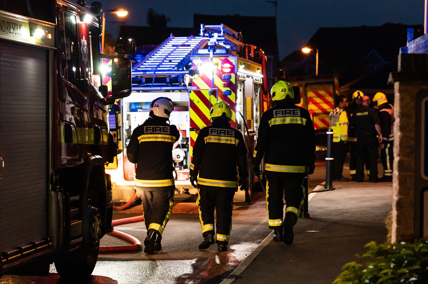 Fire fighters next to a fire engine on scene at night