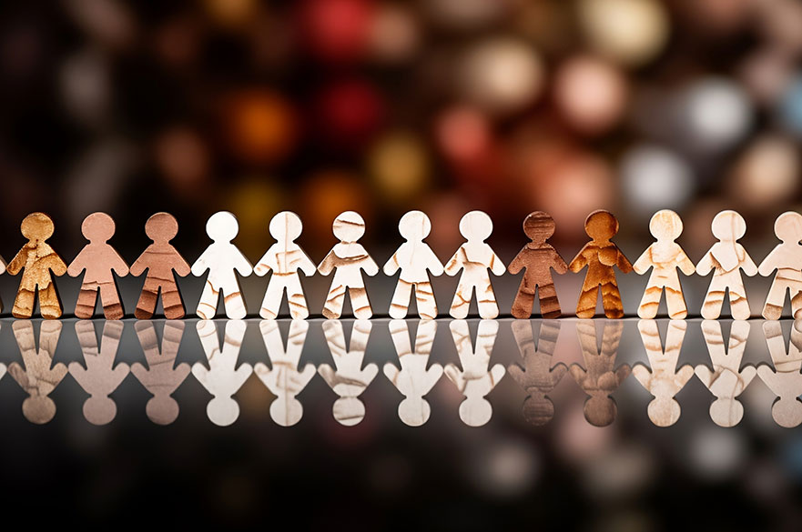 Different coloured wooden figures of people holding hands in front of christmas lights