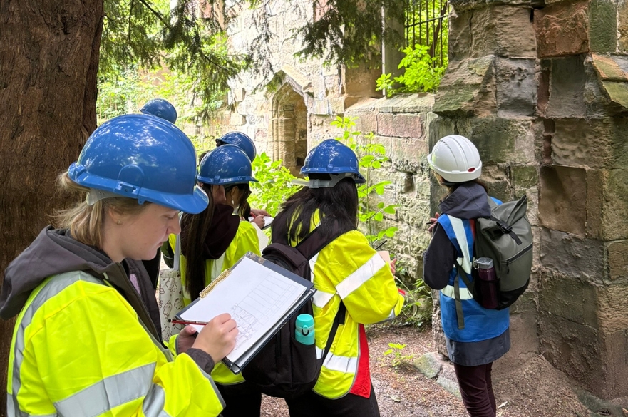 Architecture students wearing high viz's walking around the ruins of an old church.