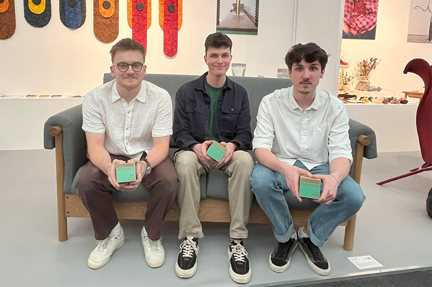 NTU students sitting down and smiling at the camera whilst holding up their awards