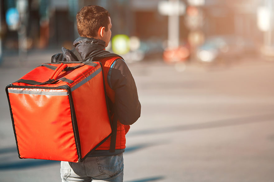 Man with a thermal food delivery box on his back walking down the street