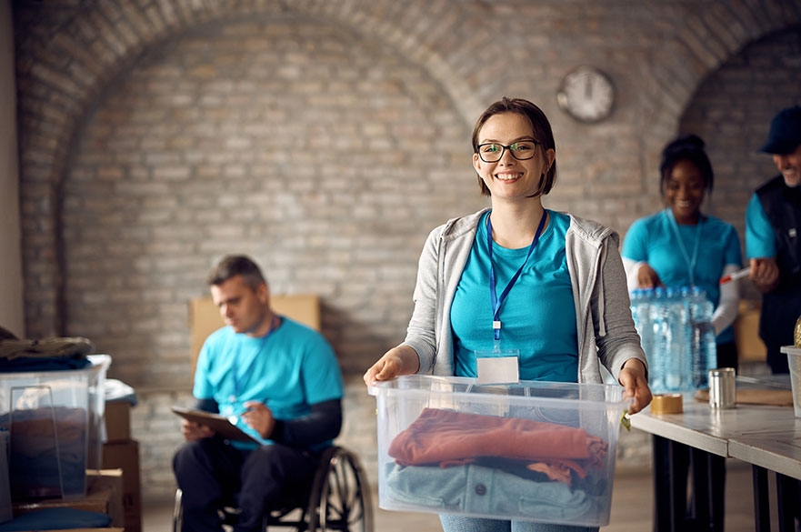 Young woman volunteer carrying a box and smiling at a donation centre