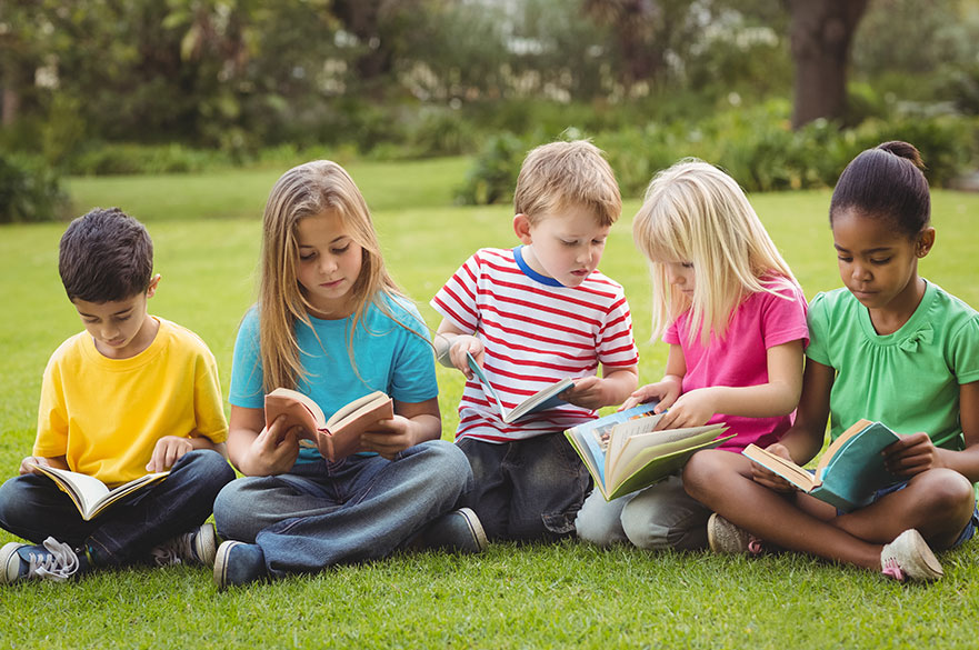 Five classmates sitting on grass and reading books