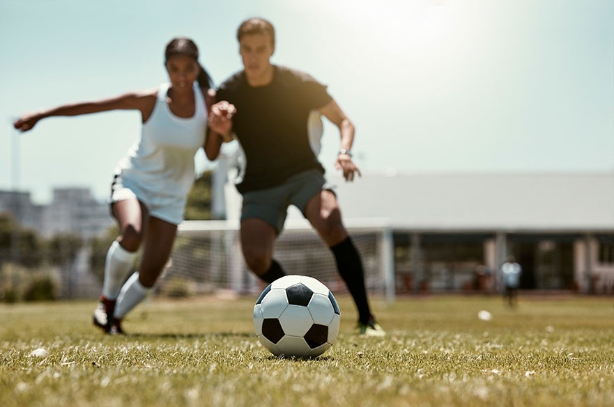 Man and woman playing football outside on a pitch
