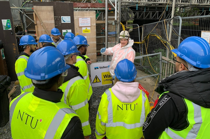 Students on site in PPE being spoken to by person in white suit