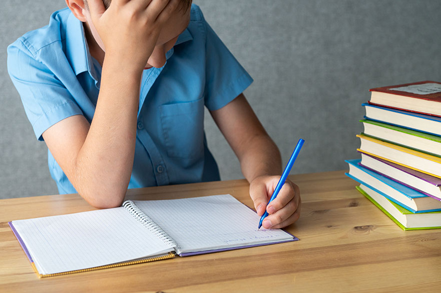 Frustrated boy in a blue shirt writing in a book