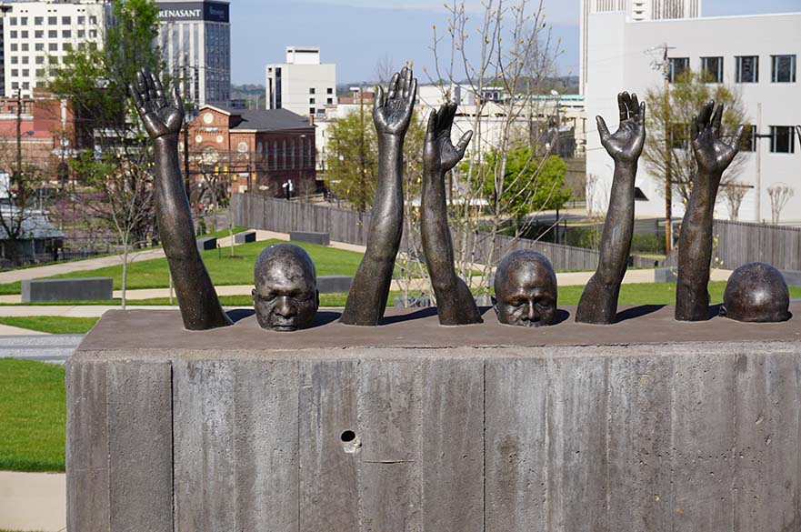 Statue of 3 men stuck in stone to their necks, with their eyes closed and arms raised in the air.