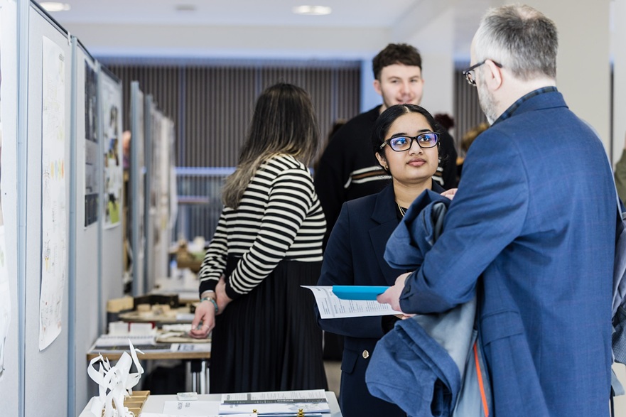 A student is at an exhibition stand listening while someone talks to her about her work