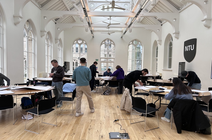 A group of students working around tables in a room.
