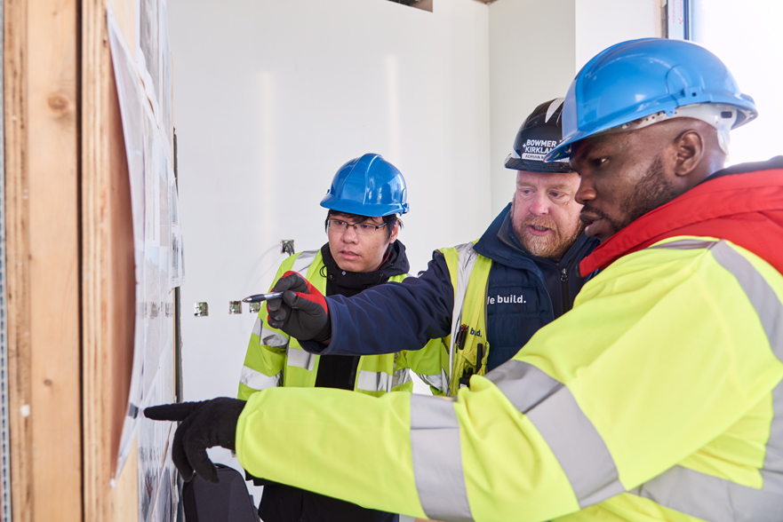 Students and employer wearing a high viz and a hard hat looking into an iPad next to some construction plans