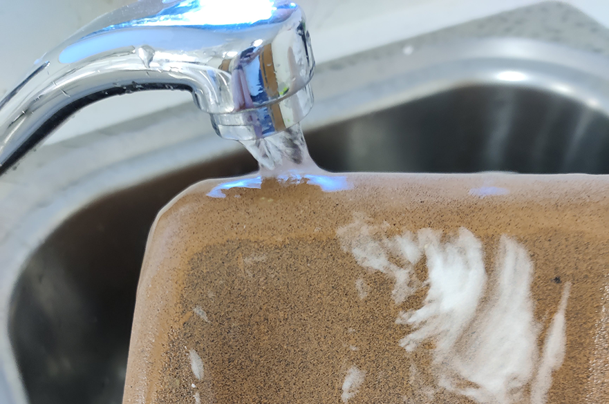 Terracotta food container being washed with water from a tap