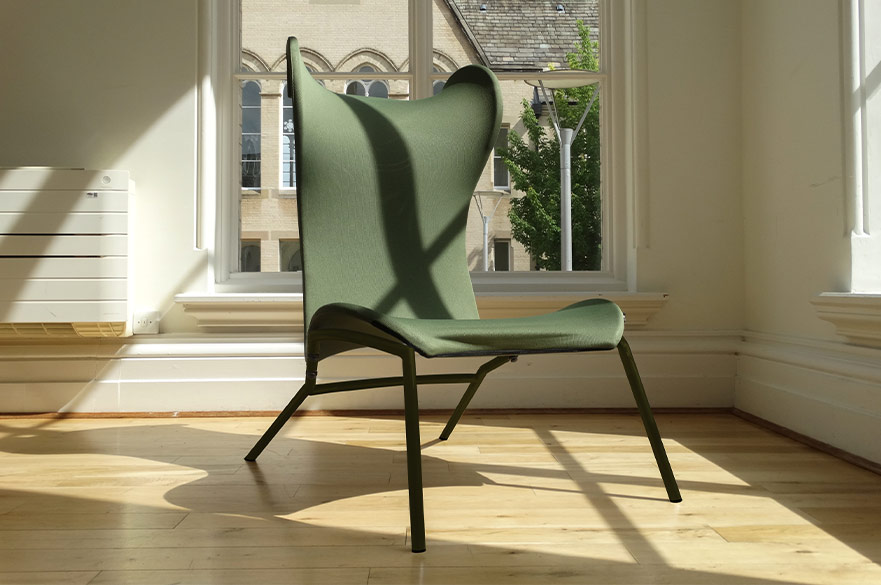 Green and wooden lounge chair displayed next to a tall window with the sun shining through