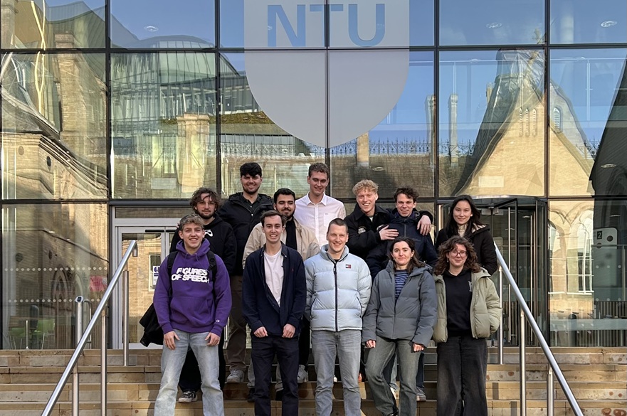 A group of students standing on the steps outside a building. They are looking at the camera.