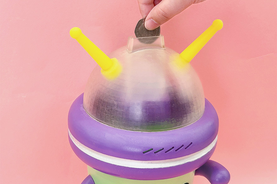 An alien shaped piggy bank with a hand inserting a coin in it