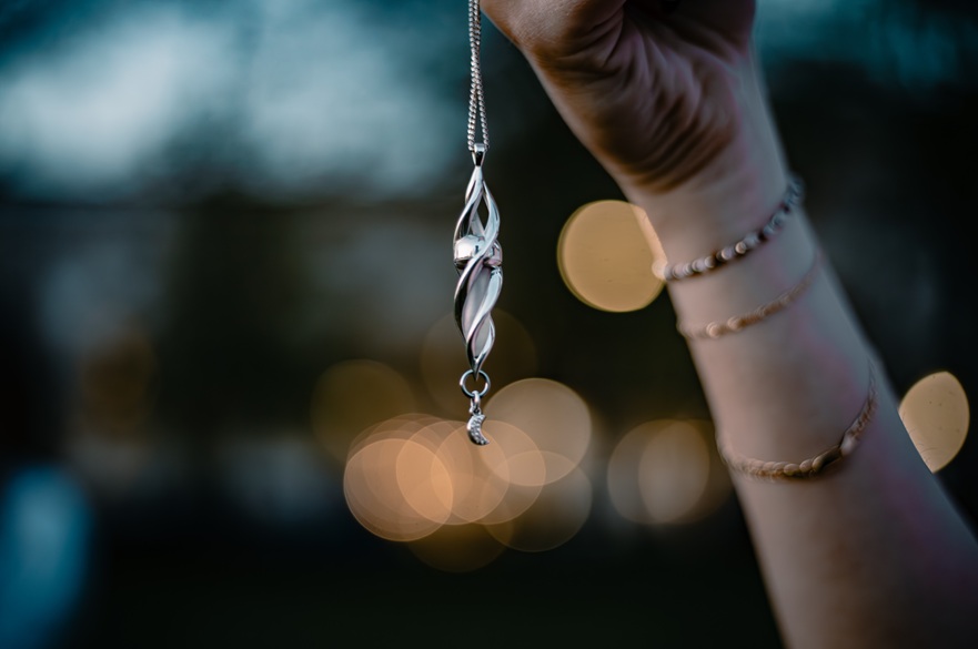 A silver-coloured pendant is being held up by a hand.