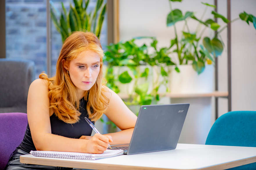 person writing on notepad looking at laptop