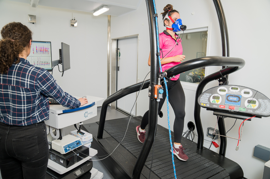 Student running on treadmill wearing a mask whilst other student observing and taking measurments 