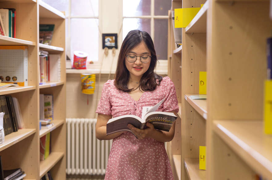 A student stood reading a book titled 'Second languages' in the library.