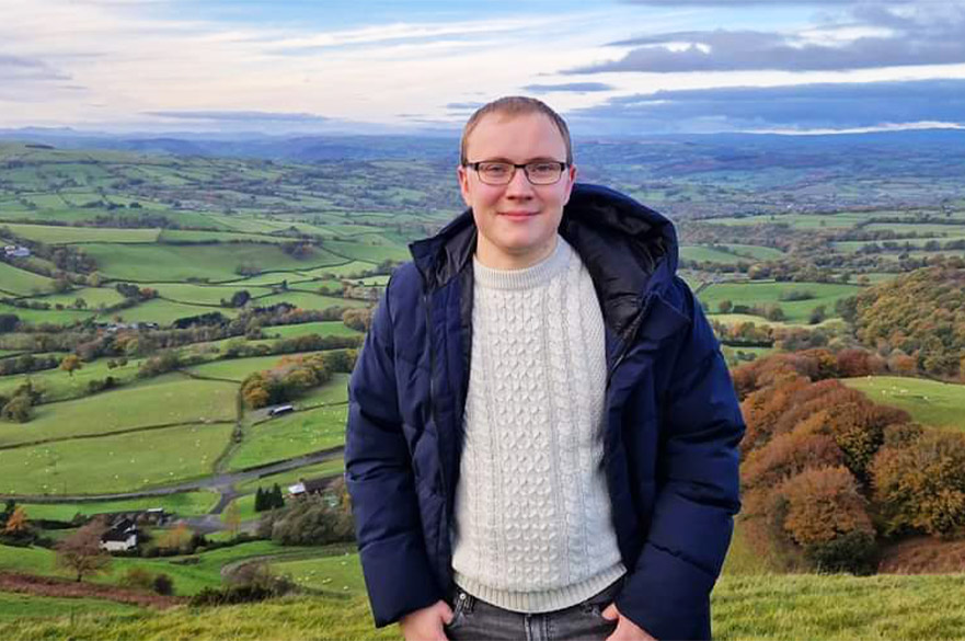 Chris smiling at the camera with the English countryside behind him