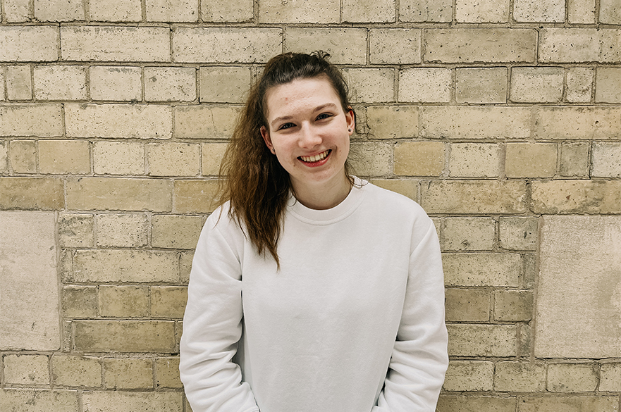 Lauren smiling at the camera in front of a brick wall