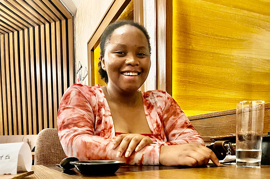 Nanfe smiling at the camera siting down in a table at a restaurant