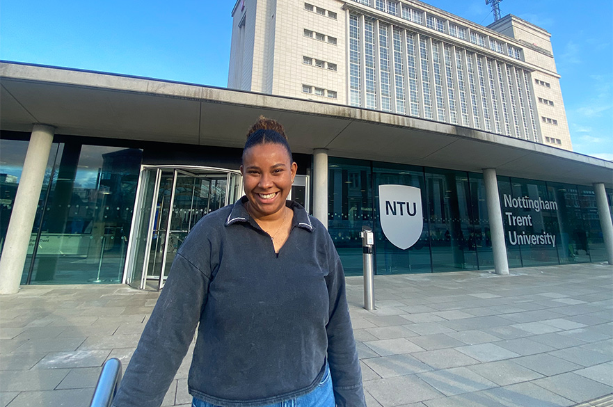 Noemie smiling at the camera standing in front of the Newton Building at NTU.