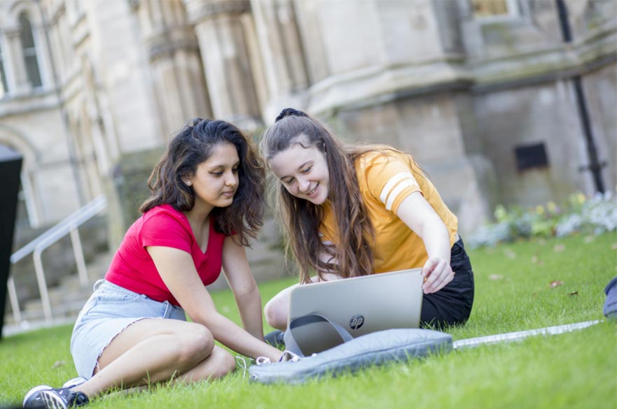 Two students looking at a laptop on the grass outside the Newton building.
