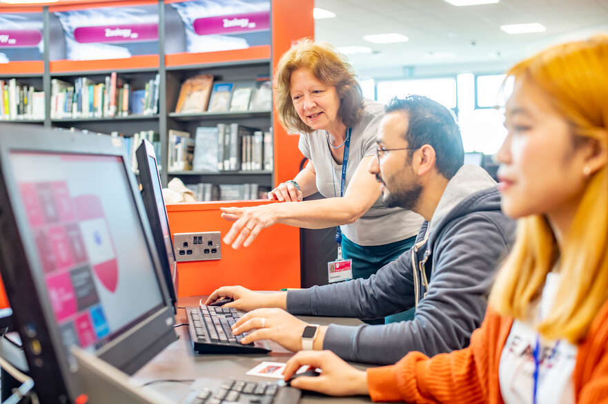 Two students studying and a staff member helping